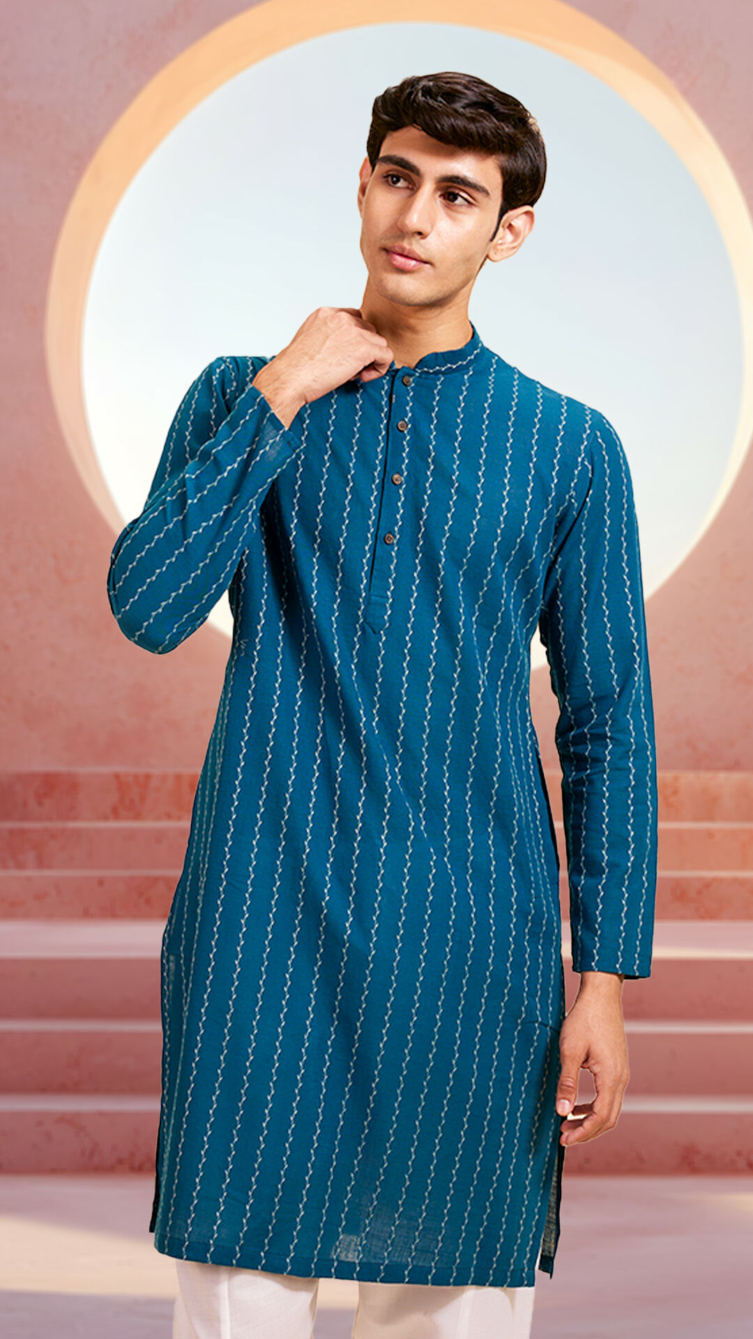 Man wearing a teal blue embroidered kurta with subtle vertical patterns, styled for festive or ethnic occasions.
